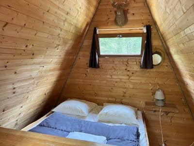 Cabane en bois à la forme triangulaire, avec un lit douillet et des murs en bois.