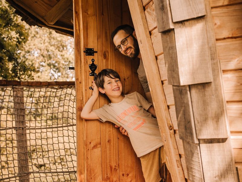 Cabane dans les arbres avec un père et son fils à la porte, ambiance chaleureuse.