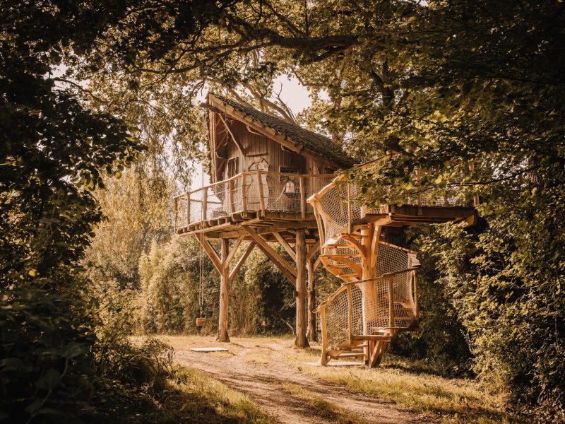 Cabane dans les arbres avec une terrasse en bois et un escalier en colimaçon.