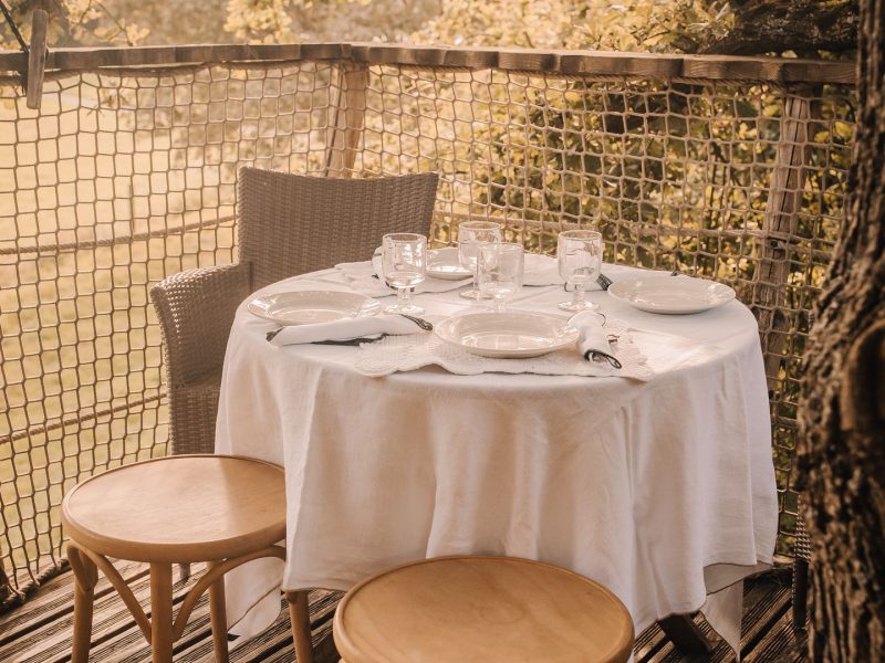 Table élégamment dressée sur une terrasse en bois, entourée de verdure.