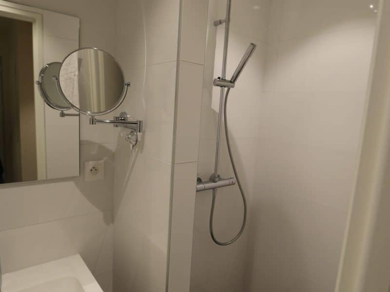 Salle de bain moderne dun hébergement touristique, avec douche à litalienne et miroir.