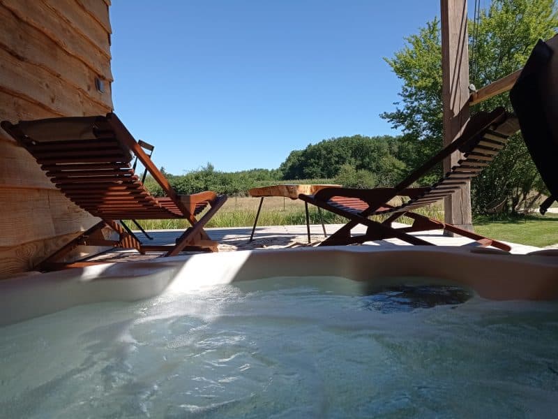 Chalet avec jacuzzi, chaises longues et vue sur la nature verdoyante.