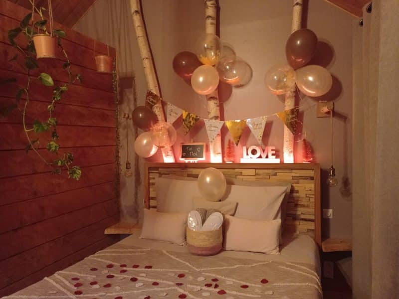 Chambre romantique avec décor de ballons et pétales de rose sur le lit.