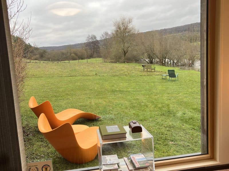 Chalet moderne avec vue sur la nature, fauteuils design et verdure apaisante.