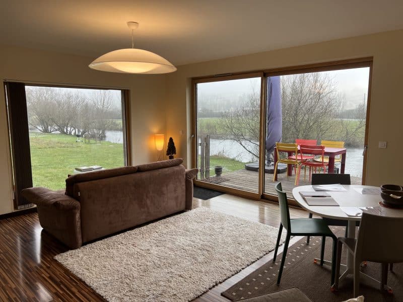 Chalet moderne avec vue sur la rivière, salon lumineux et mobilier coloré.