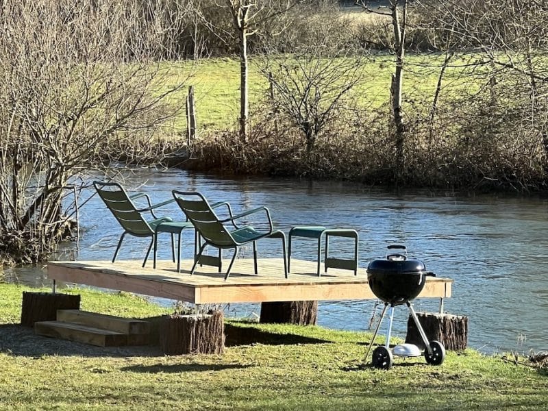 Chalet au bord de leau avec terrasse, chaises et barbecue pour des moments conviviaux.