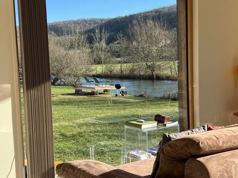 Chalet moderne avec vue sur la rivière et un jardin verdoyant.