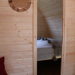 Intérieur dun hébergement insolite en bois, lit cosy et miroir rond en rotin.