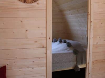 Intérieur dun hébergement insolite en bois, lit cosy et miroir rond en rotin.