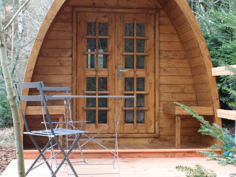 Cabane en bois en forme dœuf, avec une terrasse en bois et des chaises.