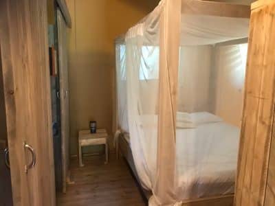 Chambre en bois avec lit à baldaquin, ambiance cosy et naturelle. Hébergement insolite.