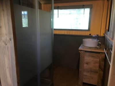Cabane moderne avec salle de bain en bois et douche vitrée, lumineuse et accueillante.