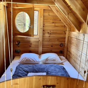 Cabane en bois cosy avec lit douillet et fenêtre ronde, située en Auvergne-Rhône-Alpes.