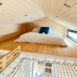 Cabane en bois avec lit douillet en mezzanine et lumière naturelle.