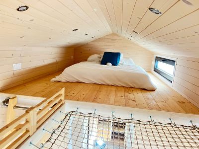 Cabane en bois avec lit douillet en mezzanine et lumière naturelle.