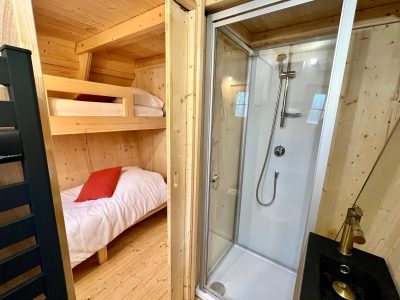 Cabane en bois avec lits superposés et salle de douche moderne. Confort naturel.