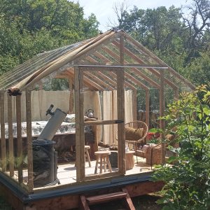 Hébergement insolite : serre en bois avec mobilier cosy, entourée de verdure.