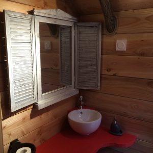 Salle de bain dun hébergement insolite en bois, avec un miroir à volets.
