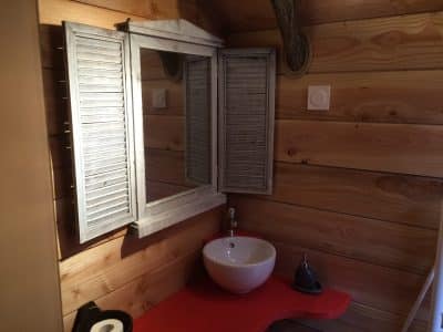 Salle de bain dun hébergement insolite en bois, avec un miroir à volets.