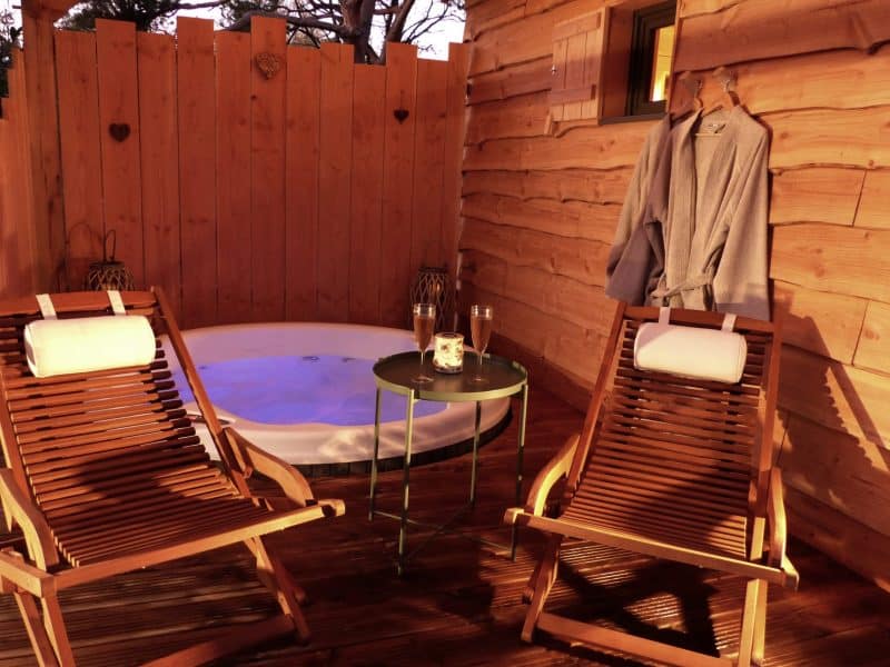 Cabane en bois avec jacuzzi, chaises longues et ambiance chaleureuse.