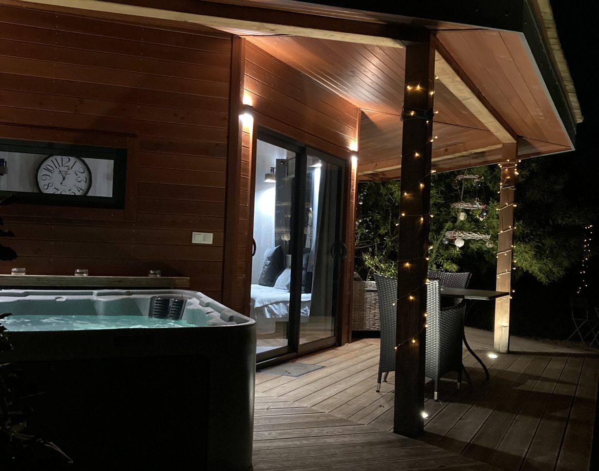 Hébergement insolite en bois avec jacuzzi, illuminé par des guirlandes lumineuses.