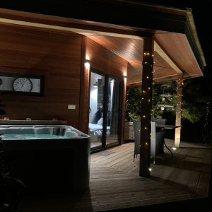 Hébergement insolite en bois avec jacuzzi, illuminé par des guirlandes lumineuses.