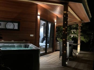 Hébergement insolite en bois avec jacuzzi, illuminé par des guirlandes lumineuses.