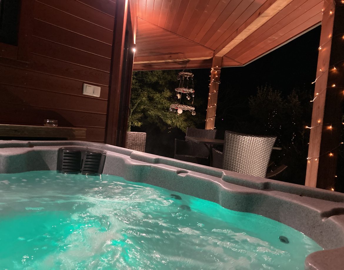 Hébergement insolite avec jacuzzi lumineux sous une terrasse en bois. Ambiance nocturne.