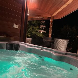 Hébergement insolite avec jacuzzi lumineux sous une terrasse en bois. Ambiance nocturne.