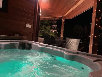 Hébergement insolite avec jacuzzi lumineux sous une terrasse en bois. Ambiance nocturne.