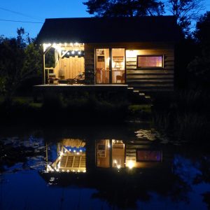 Cabane en bois au bord dun étang, illuminée par des guirlandes lumineuses.