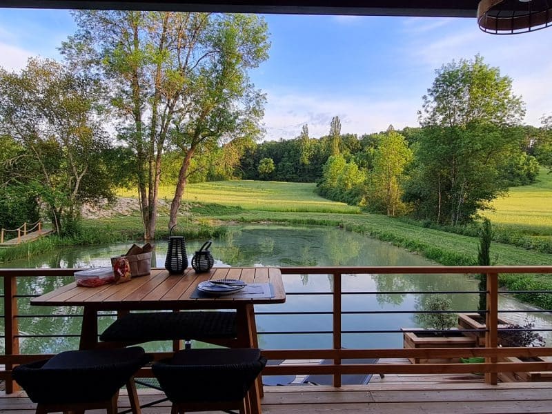 Chalet au bord de leau, avec une terrasse en bois offrant une vue sur la nature verdoyante.