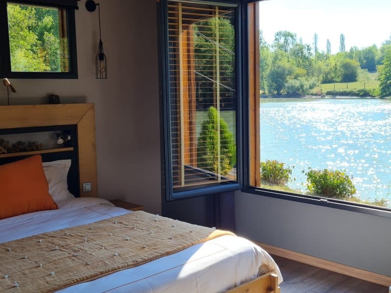 Chambre dhôtes moderne avec vue sur un lac scintillant et verdure environnante.