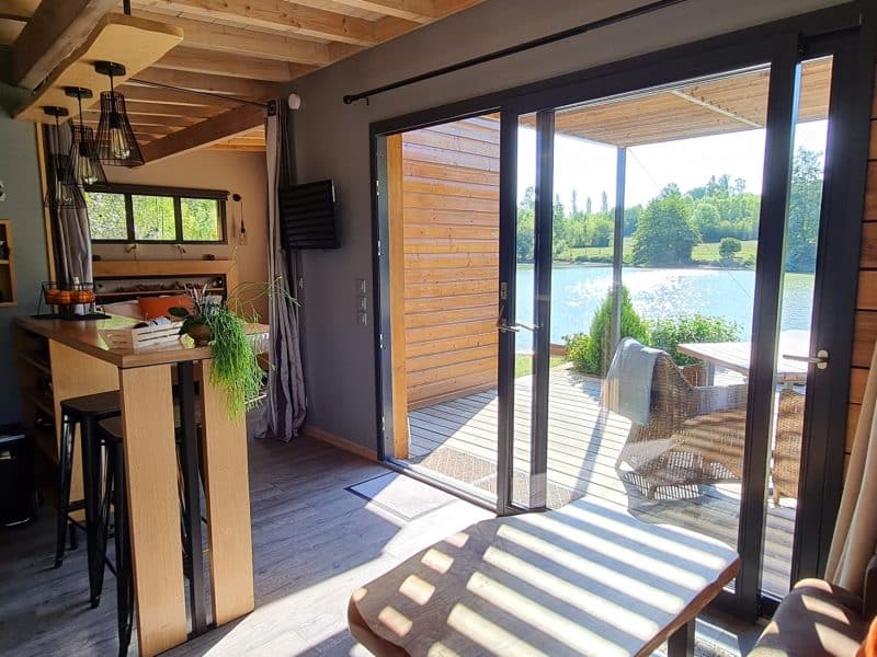 Chalet moderne avec vue sur lac, terrasse en bois et intérieur chaleureux.