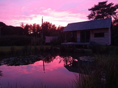 Cabane en bois au bord dun étang, reflet du ciel rose au coucher de soleil.