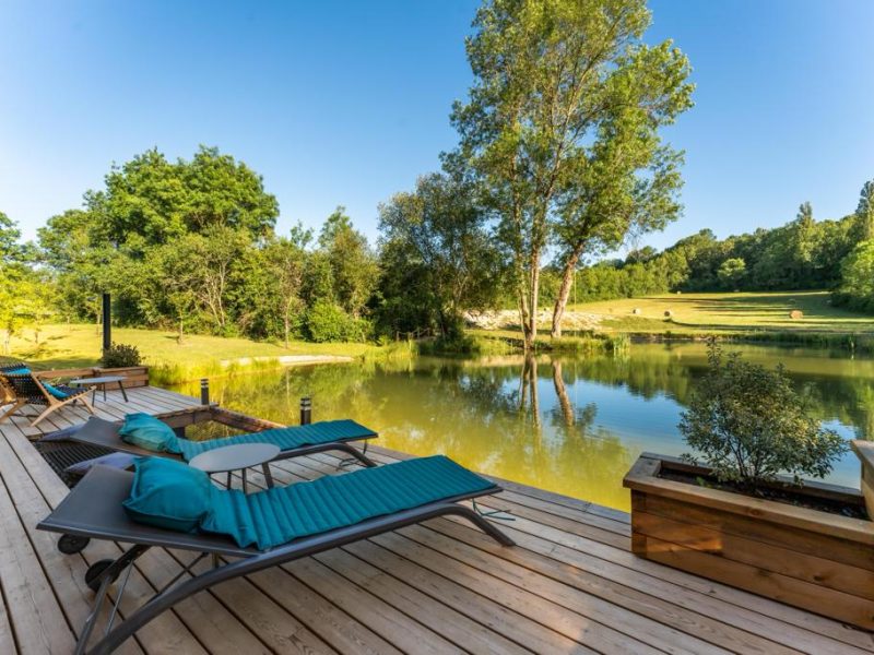 Chalet au bord dun lac, avec chaises longues sur une terrasse en bois.