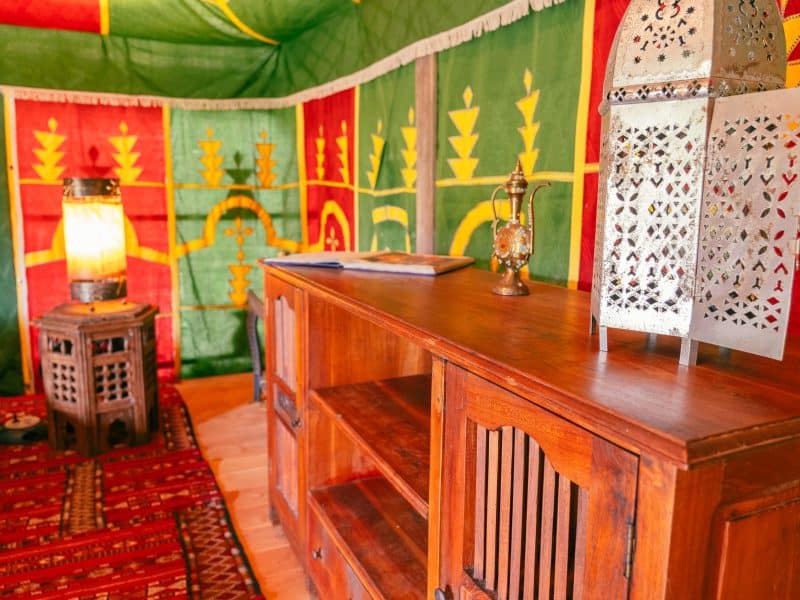 Tente berbère chaleureuse avec décor coloré et mobilier en bois traditionnel.