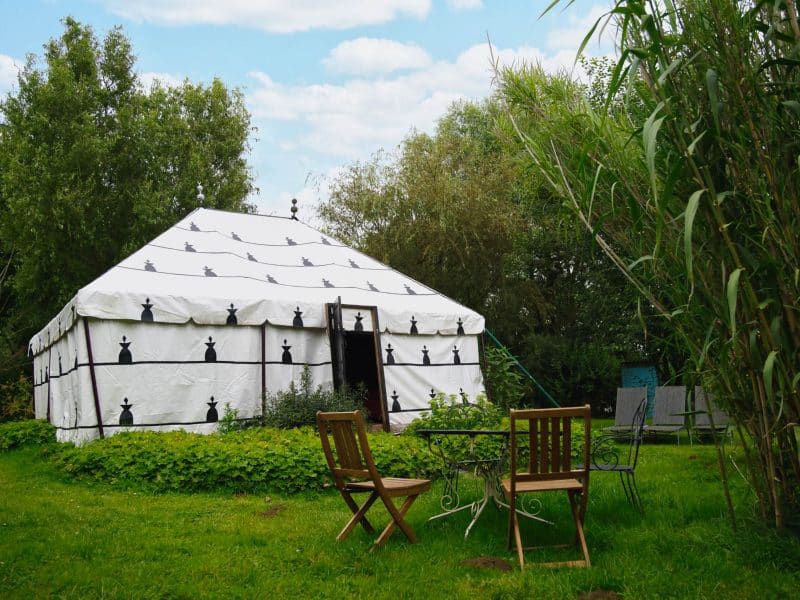 Yourte spacieuse dans un jardin verdoyant, avec chaises en bois à lextérieur.
