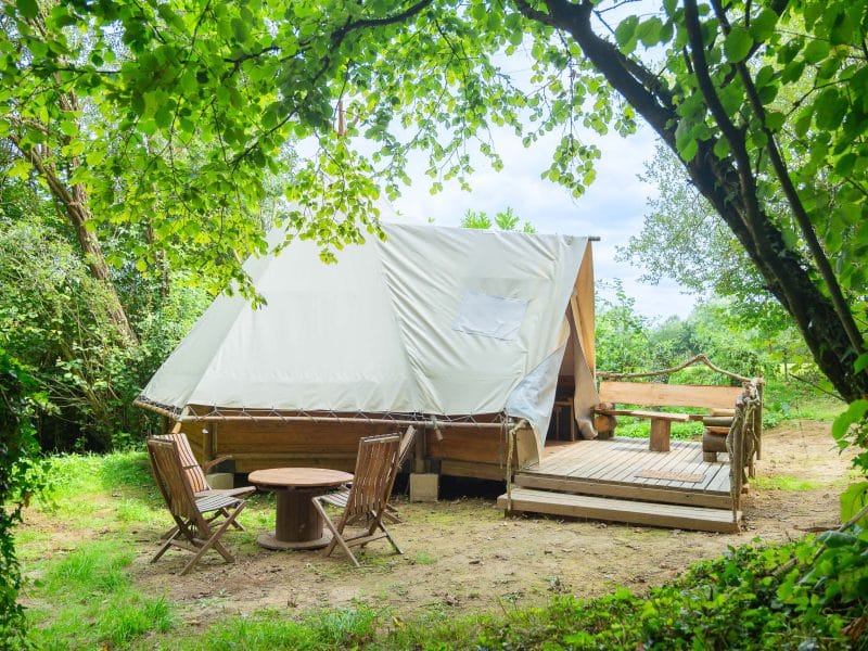 Tente safari en pleine nature, avec terrasse en bois et chaises confortables.