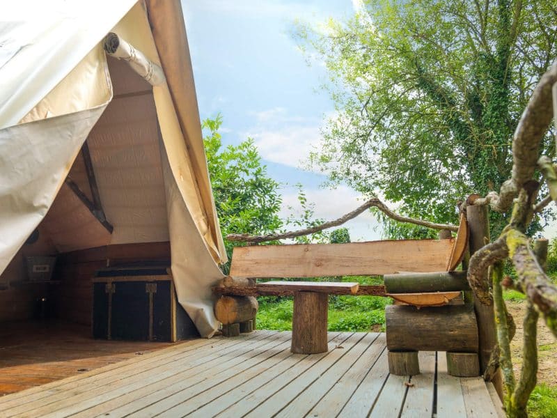 Tente safari avec terrasse en bois, entourée de verdure paisible.