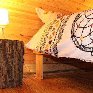 Chalet en bois avec lit douillet et lampe sur un tronc darbre. Ambiance chaleureuse.