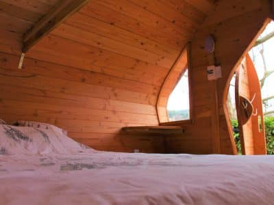Cabane en bois avec lit confortable et grandes fenêtres offrant une vue sur la nature.