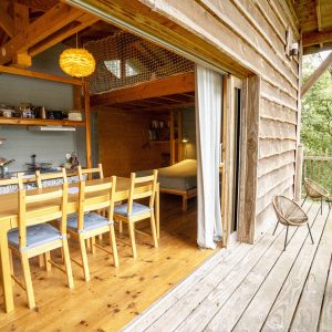 Cabane en bois dans les arbres avec vue sur la nature et espace repas lumineux.