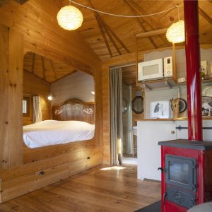 Cabane en bois avec lit douillet et poêle à bois, ambiance chaleureuse et naturelle.