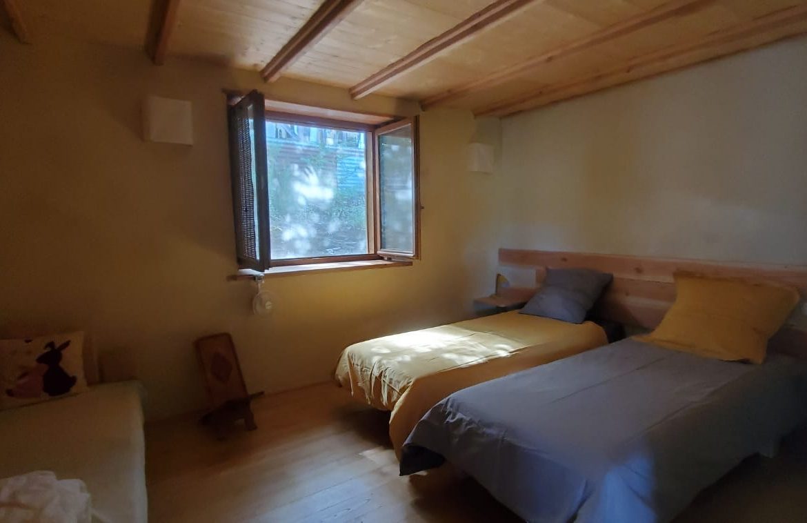 Chalet en bois lumineux avec lits simples et fenêtres ouvertes sur la nature.