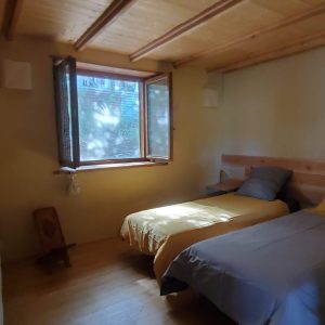 Chalet en bois lumineux avec lits simples et fenêtres ouvertes sur la nature.