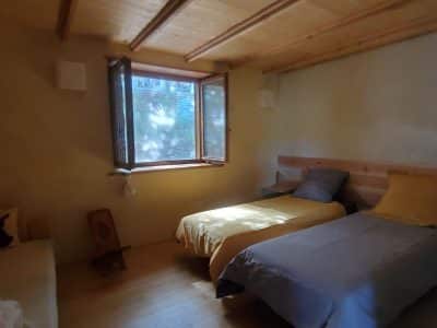 Chalet en bois lumineux avec lits simples et fenêtres ouvertes sur la nature.