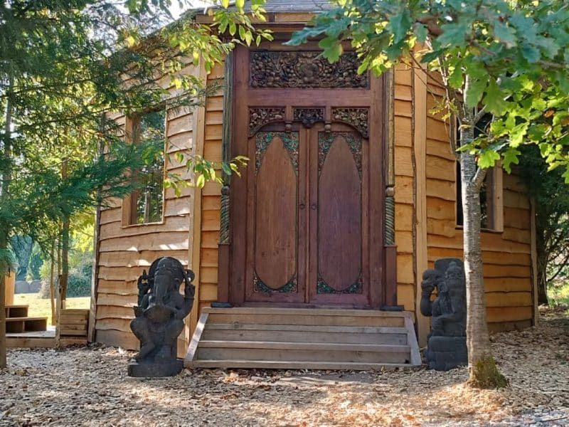 Cabane en bois avec une porte sculptée, nichée dans la verdure des Pays de la Loire.
