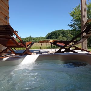 Hébergement insolite avec jacuzzi, chaises longues et vue sur la nature verdoyante.