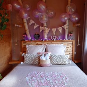 Chalet romantique avec lit décoré de pétales en forme de cœur et ballons.